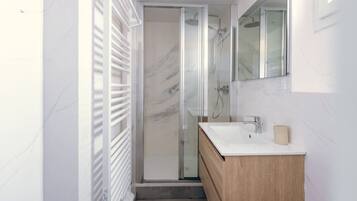 Een moderne badkamer met een douchecabine van glas, een houten wastafelmeubel en een wand betegeld met marmer.
