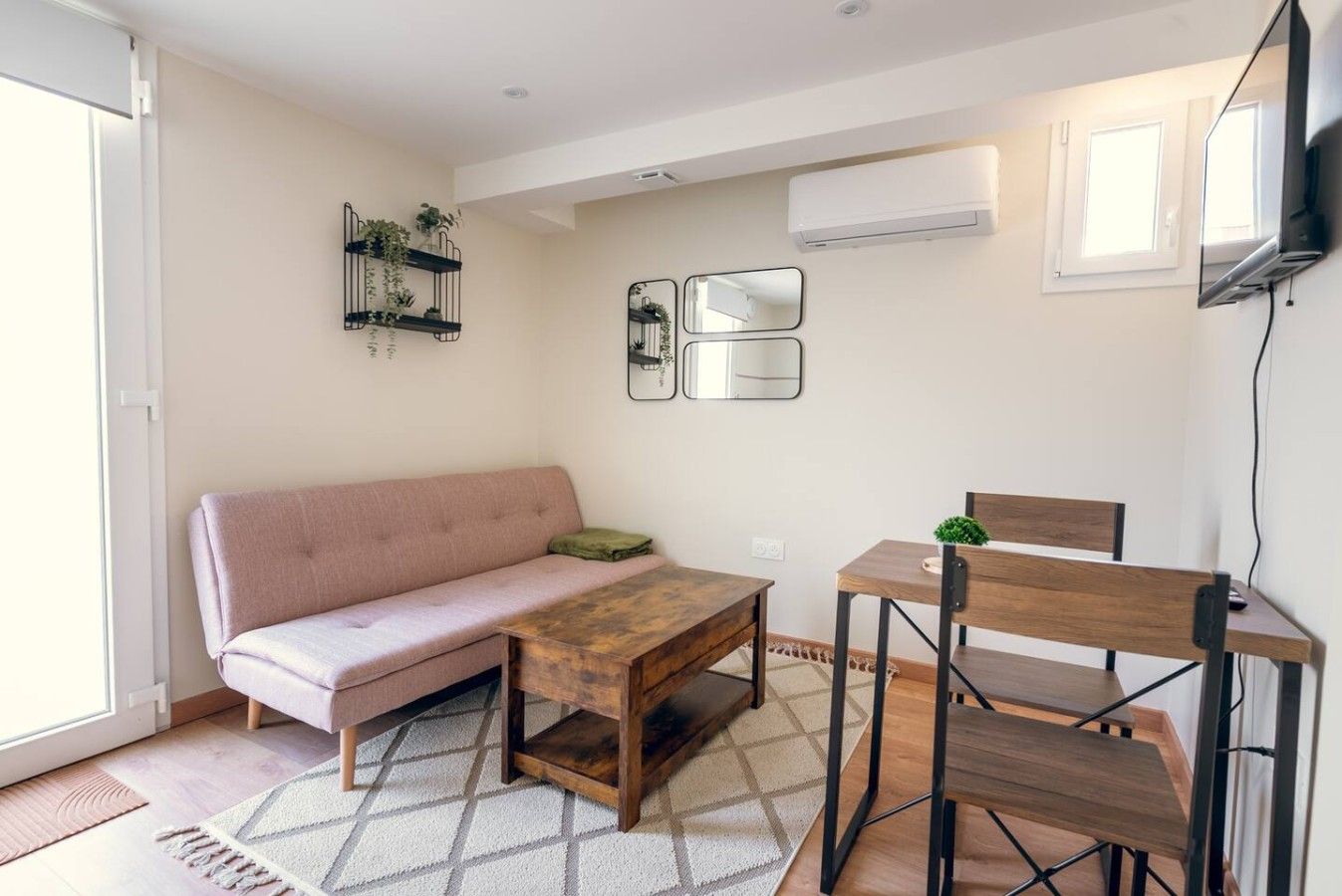 Een woonkamer met een bank, een houten tafel en een stoel. Op de tafel staat een klein plantje en aan de muur hangt een spiegel.