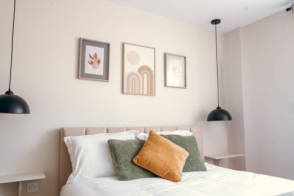 Une chambre à coucher bien rangée, avec un lit, des oreillers et des œuvres d’art accrochées au mur.