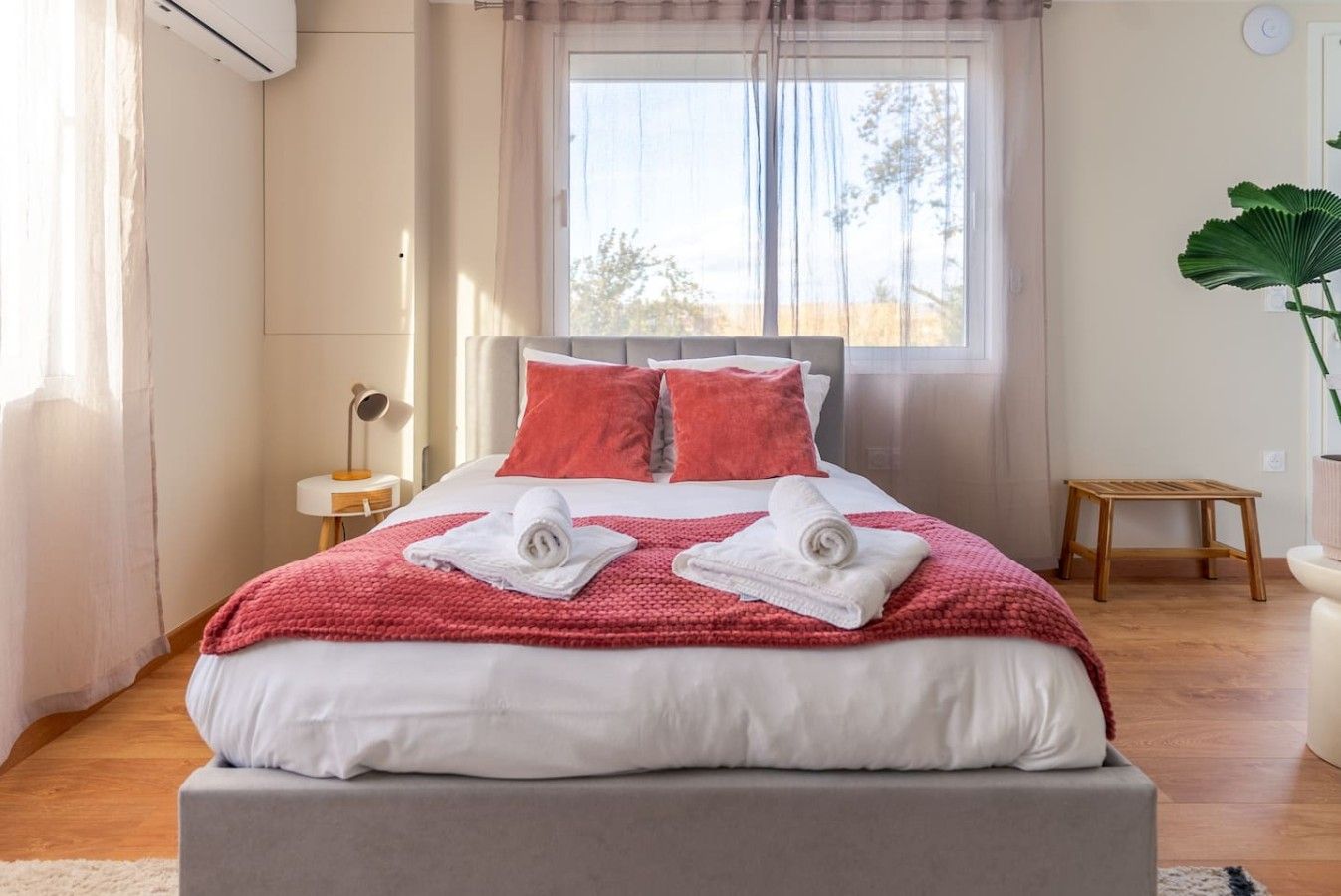 Une chambre d’hôtel avec un lit, une table de chevet, une lampe, une fenêtre avec des rideaux et une plante en pot.