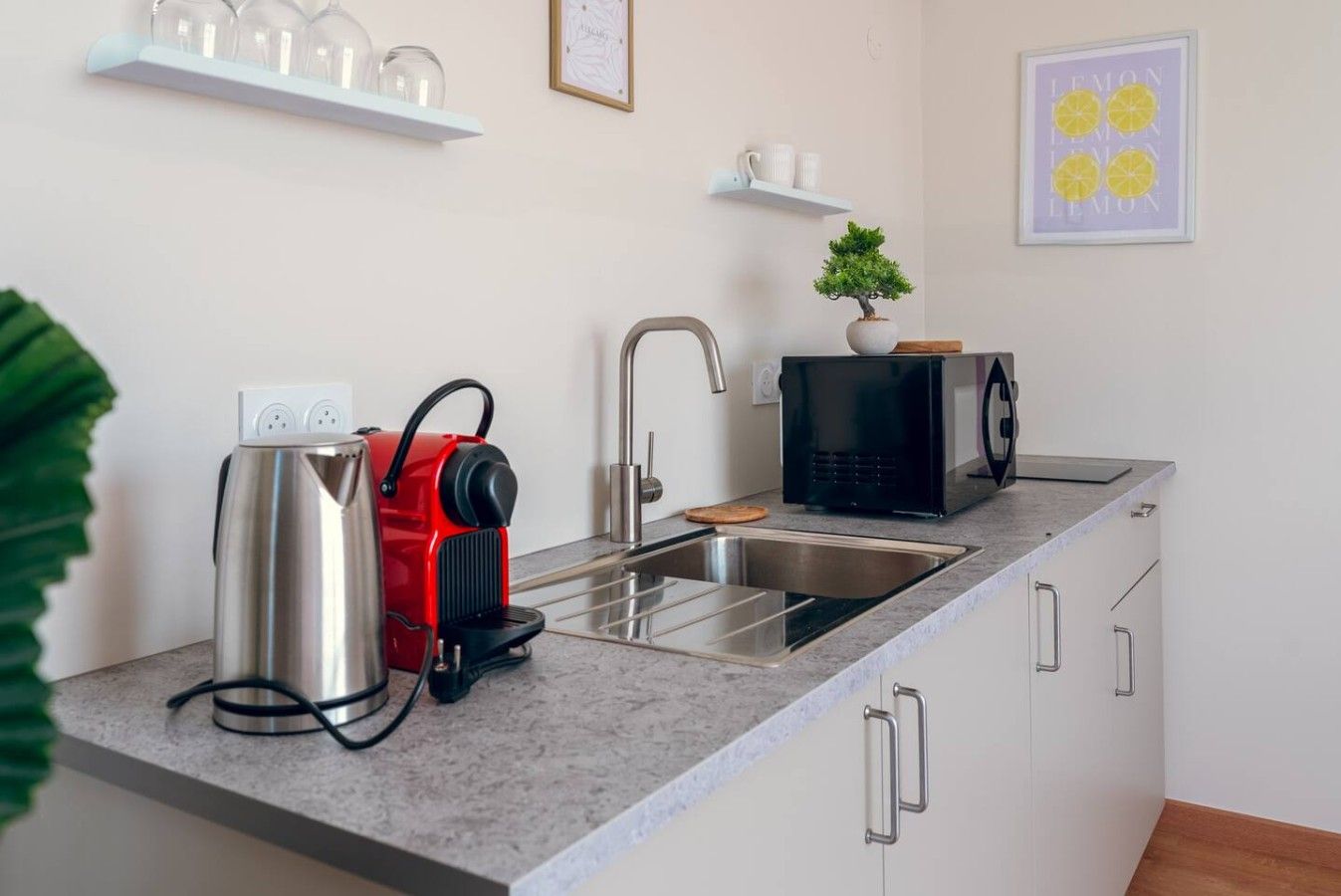 Een moderne keuken met een roestvrijstalen waterkoker, een zwarte magnetron en een spoelbak.