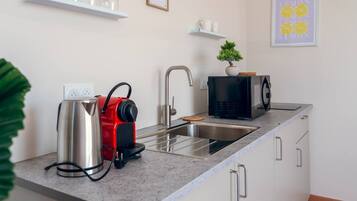 Een moderne keuken met een roestvrijstalen waterkoker, een zwarte magnetron en een spoelbak.
