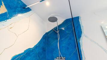 Een moderne badkamer met een grote blauwe marmeren wand, een in het plafond gemonteerde douchekop en zichtbare leidingen.