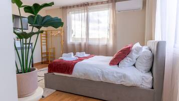 Een slaapkamer met een bed, een televisie, een plant en een raam met gordijnen.
