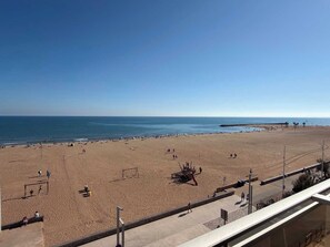 Une plage avec un ciel dégagé, un rivage sablonneux et quelques personnes.