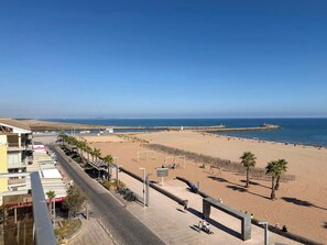 A beach with a clear sky, a promenade with shops, and a distant view of the sea. - Stunning Beachfront 3 Bedroom Apartment in Valras Plage with Balcony (Valras-Plage)