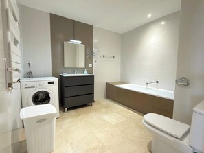 A modern bathroom with a washing machine, a dark-colored vanity, a bathtub, and a toilet. - Stunning Beachfront 3 Bedroom Apartment in Valras Plage with Balcony (Valras-Plage)