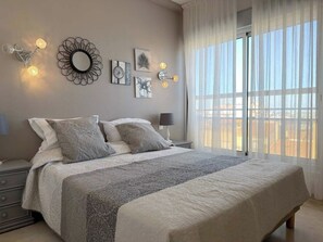 A bedroom with a bed, bedside tables, wall art, and a window with curtains. - Stunning Beachfront 3 Bedroom Apartment in Valras Plage with Balcony (Valras-Plage)