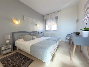 Quarto com cama, mesas de cabeceira, escrivaninha e uma cadeira.