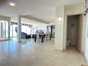 A spacious living area with a dining table and chairs, a sofa, and a view through a glass door. - Beachfront 3 Bedroom Apartment with Panoramic Sea View and Balcony (Valras-Plage)