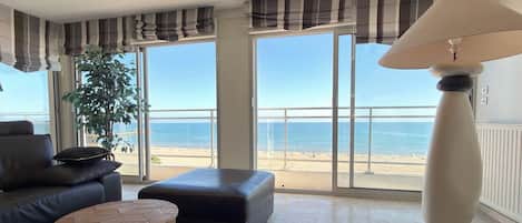 A modern living room with a view of the beach, a sofa, a round coffee table, and a floor lamp.