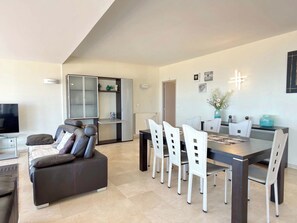A modern living room with a sofa, a dining table with chairs, and a television. - Beachfront 3 Bedroom Apartment with Panoramic Sea View and Balcony (Valras-Plage)