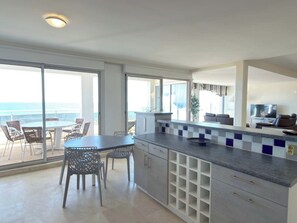A modern kitchen with a large island, a dining area with chairs, and a view of the ocean. - Beachfront 3 Bedroom Apartment with Panoramic Sea View and Balcony (Valras-Plage)
