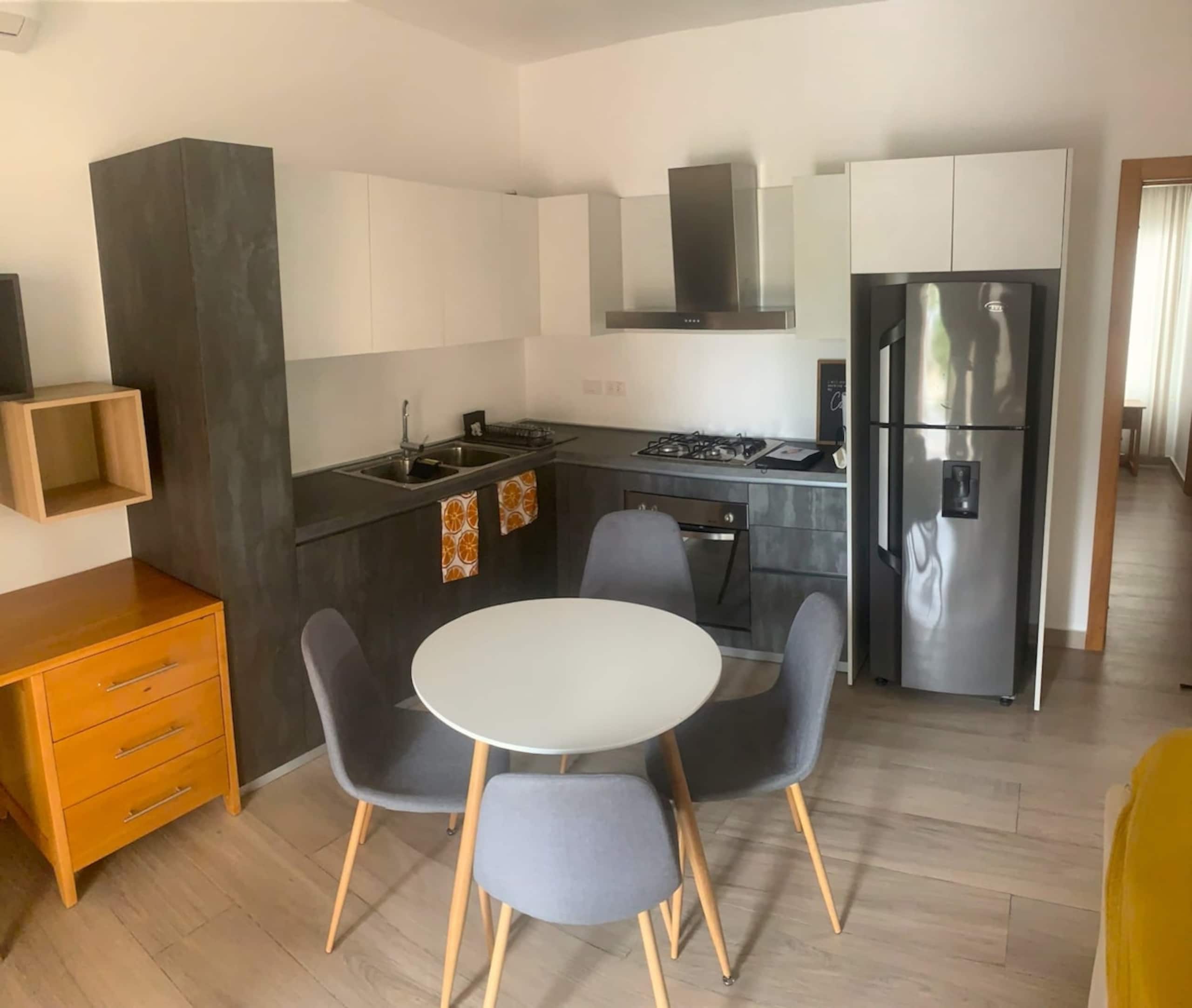 A modern kitchen with a gas stove, stainless steel refrigerator, and a dining area with a round table and two chairs.