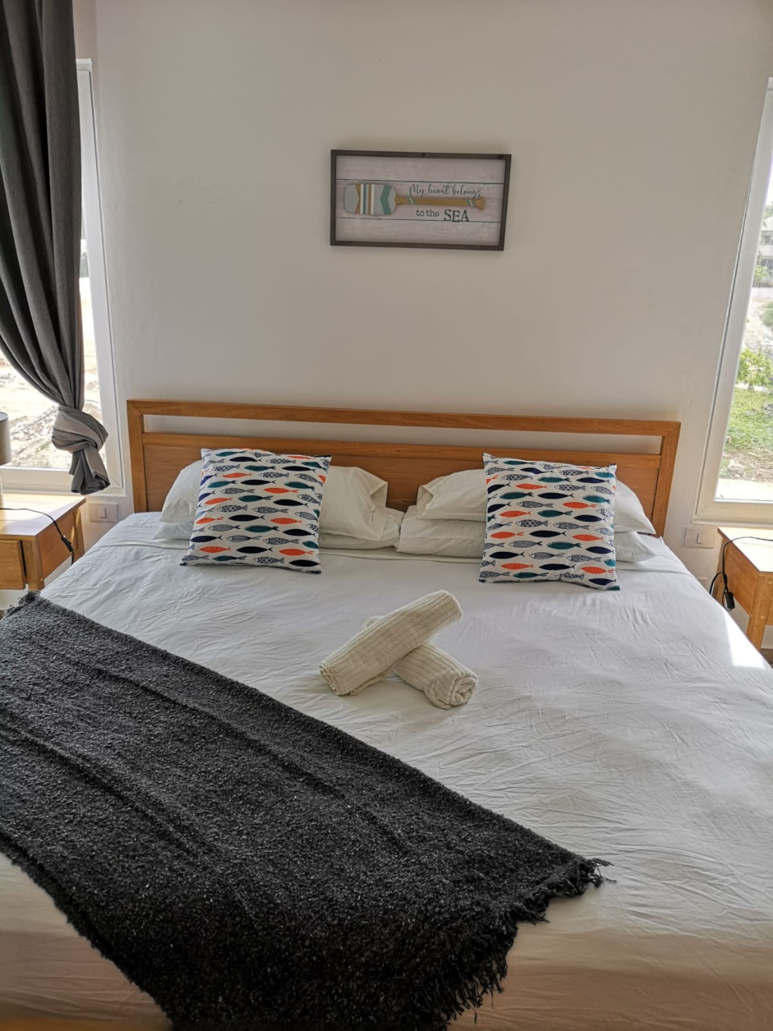 Una cama bien hecha con dos almohadas, una toalla enrollada y un cuadro en la pared.