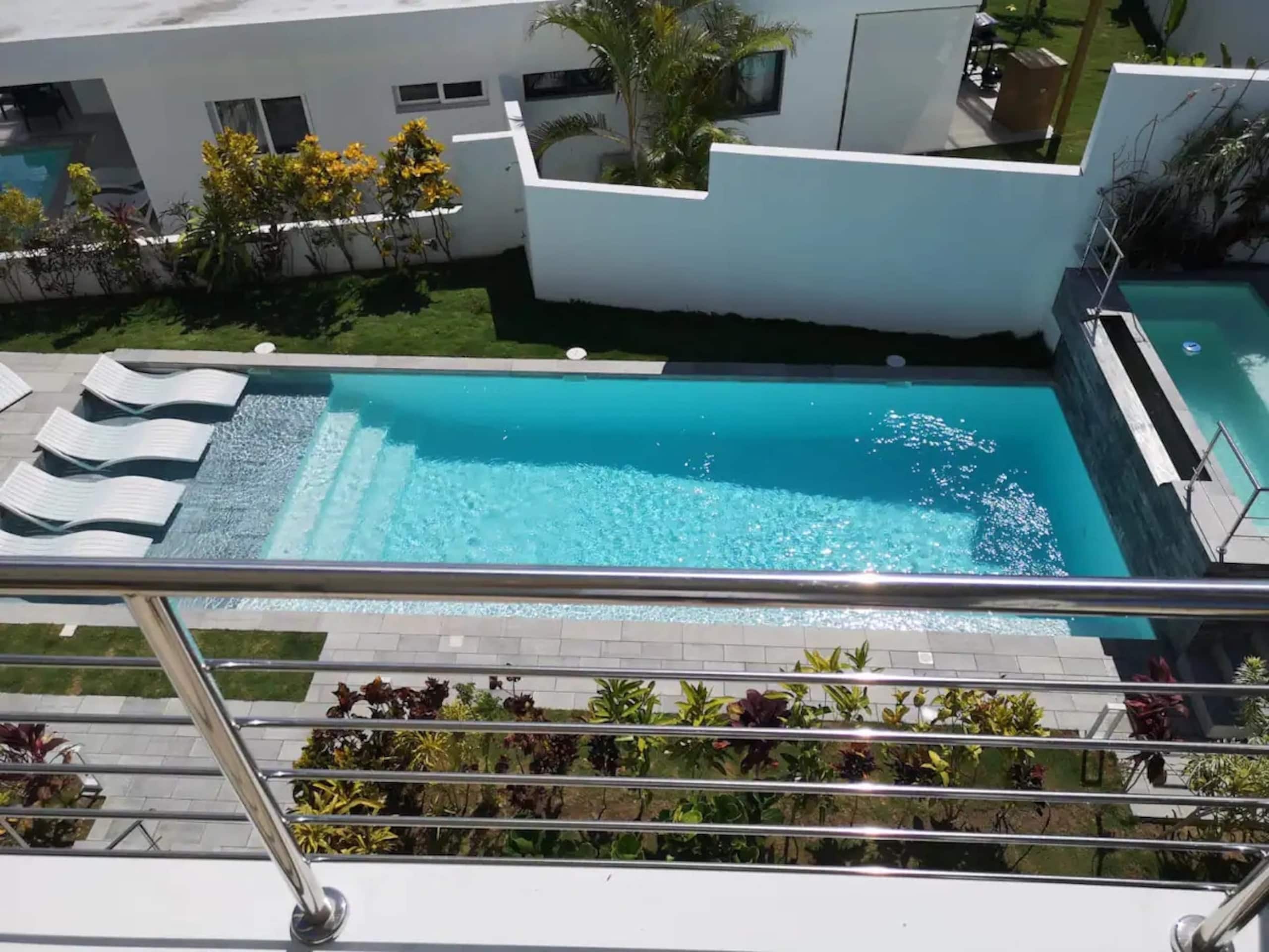Een zwembad met een modern ontwerp, omringd door een verzorgde tuin en een wit gebouw.