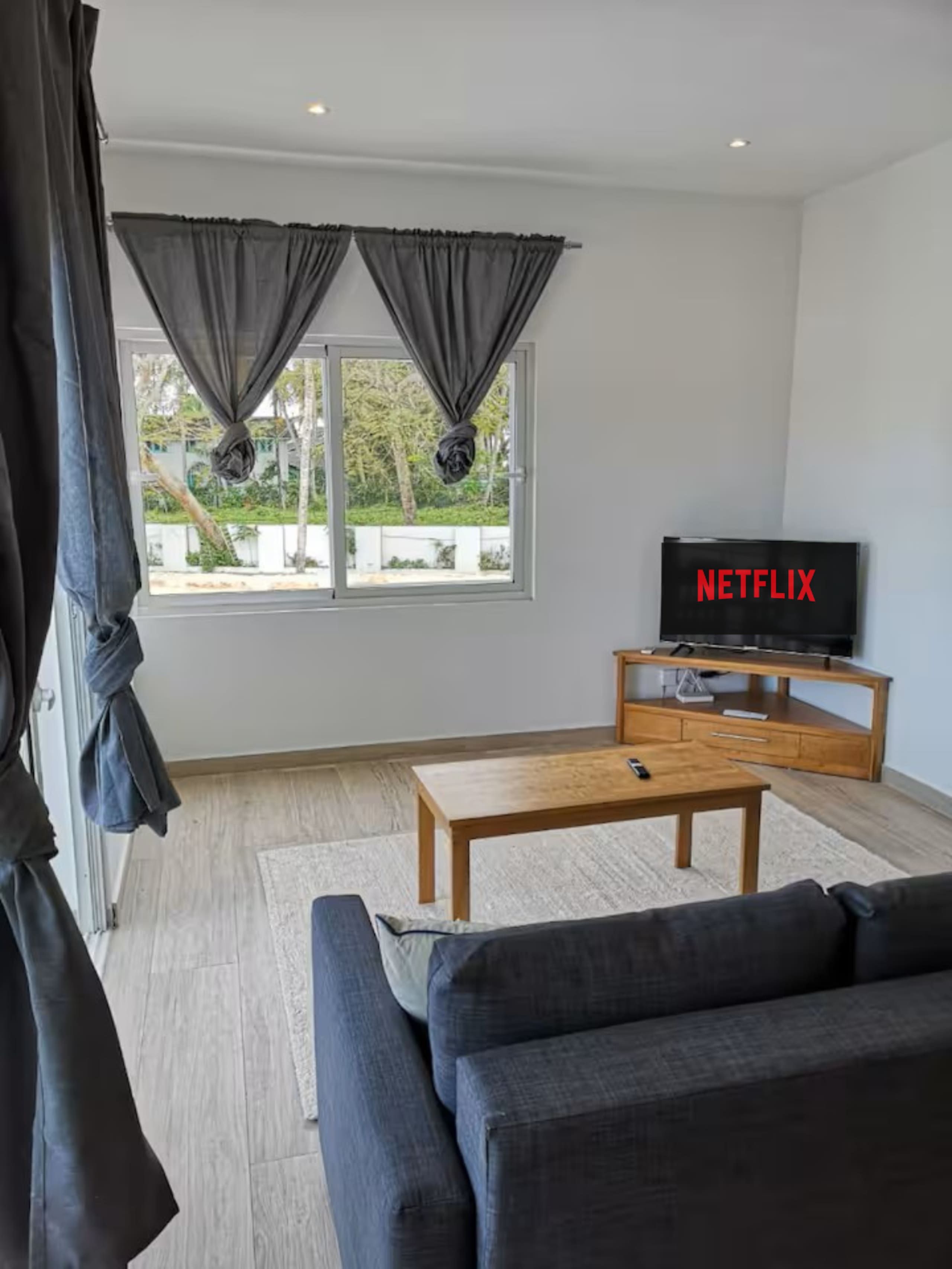 A modern living room with a sofa, a coffee table, a TV, and a window with curtains.