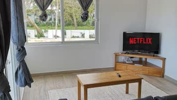 A modern living room with a sofa, a coffee table, a TV, and a window with curtains.