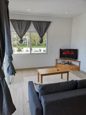 A modern living room with a sofa, a coffee table, a TV, and a window with curtains. - Case Damare Coralstone 2 (Las Terrenas)