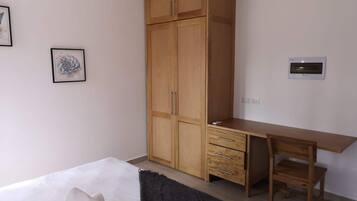 Een slaapkamer met een bed, een houten kledingkast, een bureau met een stoel en een wandairconditioner.