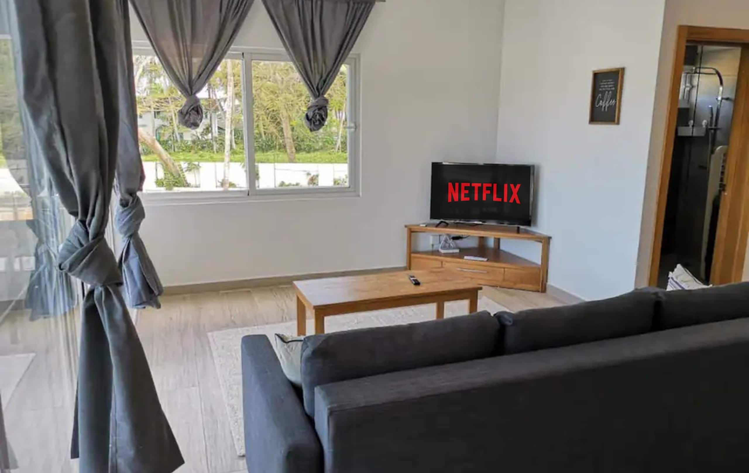 Een woonkamer met een bank, een salontafel, een tv op een meubel en een raam met gordijnen.