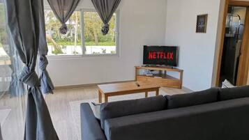 Een woonkamer met een bank, een salontafel, een tv op een meubel en een raam met gordijnen.