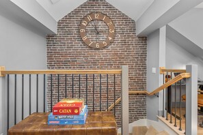 A staircase with a wooden handrail and a metal railing, leading to a room with a brick wall and a large clock. - Historic Bay Village / Cozy 1BR Getaway (Boston)