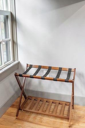 Ein hölzerner Kleiderständer mit zwei Ablageflächen, vor einer weißen Wand mit einem Fenster links.
