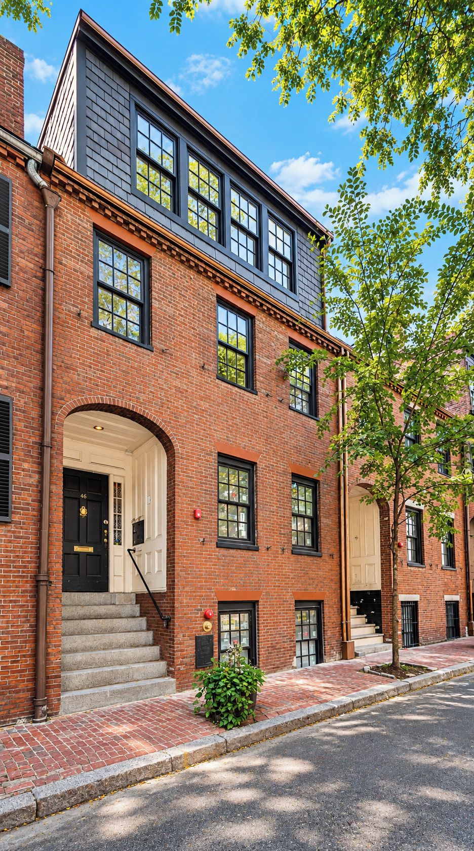 A multi-story brick building with a black door, windows, and a small garden area.