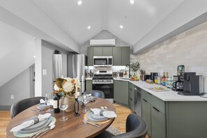 A modern kitchen with a dining area, featuring a wooden table set for a meal, a built-in oven, and a coffee machine. - Historic Bay Village / Cozy 1BR Getaway (Boston)