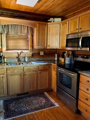 Eine Küche mit Holzausstattung, einem Edelstahlspülbecken, einer Mikrowelle und einem Backofen.