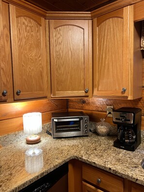 A kitchen with wooden cabinets, a toaster oven, a coffee maker, and a lamp on the countertop. - Peaceful 3 BR + Loft river-front cabin close to Lake Lure, Chimney Rock, TIEC. (Rutherfordton)