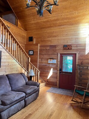 A wooden interior with a staircase, a red door, a wooden dresser, and a leather sofa. - Peaceful 3 BR + Loft river-front cabin close to Lake Lure, Chimney Rock, TIEC. (Rutherfordton)