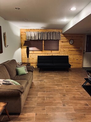 Ein Wohnzimmer mit Holzboden, einer Couch, einer Lampe und einem Fenster mit Jalousien.