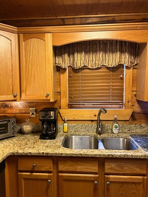 A kitchen with wooden cabinets, a granite countertop, a built-in oven, a coffee maker, and a stainless steel sink. - Peaceful 3 BR + Loft river-front cabin close to Lake Lure, Chimney Rock, TIEC. (Rutherfordton)
