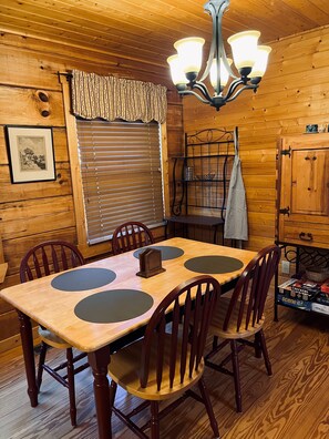 A wooden interior with a dining table, chairs, a chandelier, and a window with blinds. - Peaceful 3 BR + Loft river-front cabin close to Lake Lure, Chimney Rock, TIEC. (Rutherfordton)
