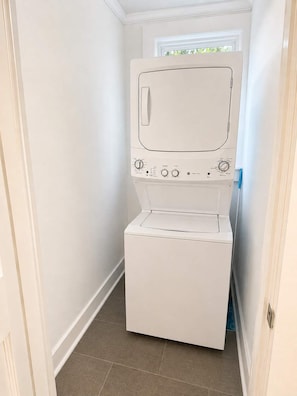 A compact, white laundry room with a built-in washer and dryer, a small window, and a tiled floor. - Park Avenue Retreat | Near Downtown (Savannah)