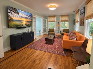 A living room with a flat-screen TV, a dark-colored cabinet, an orange sofa, and a patterned rug. - Park Avenue Retreat | Near Downtown (Savannah)