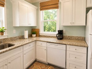 A kitchen with white cabinets, a granite countertop, a coffee maker, and a window with a view of greenery. - Park Avenue Retreat | Near Downtown (Savannah)