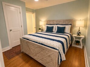 A bedroom with a bed, two bedside tables with lamps, a door, and a wooden floor. - Park Avenue Retreat | Near Downtown (Savannah)