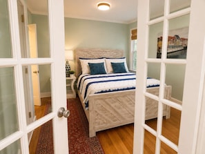 A bedroom with a bed, bedside tables, a nightstand, and a window with a view of buildings. - Park Avenue Retreat | Near Downtown (Savannah)