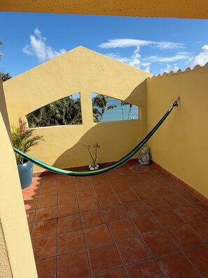 Eine mit Fliesen ausgelegte Terrasse mit einer Hängematte, einem kleinen Topfpflanzen und einem an der Wand befestigten Haken.