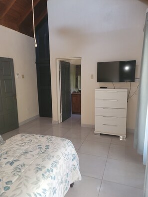 Una camera da letto con un letto, una cassettiera, un televisore e una porta che dà su un'altra stanza.