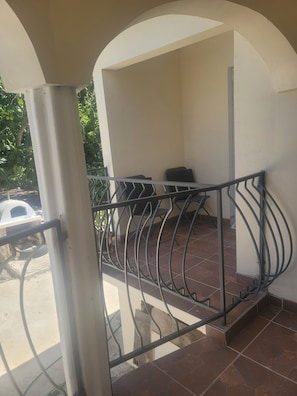 Un balcone con ringhiera in metallo, pavimento piastrellato e parete bianca.