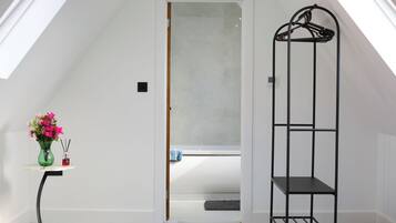 A room with a sloped ceiling, a door leading to a bathroom, a black metal shelf, and a small table with a vase of flowers.