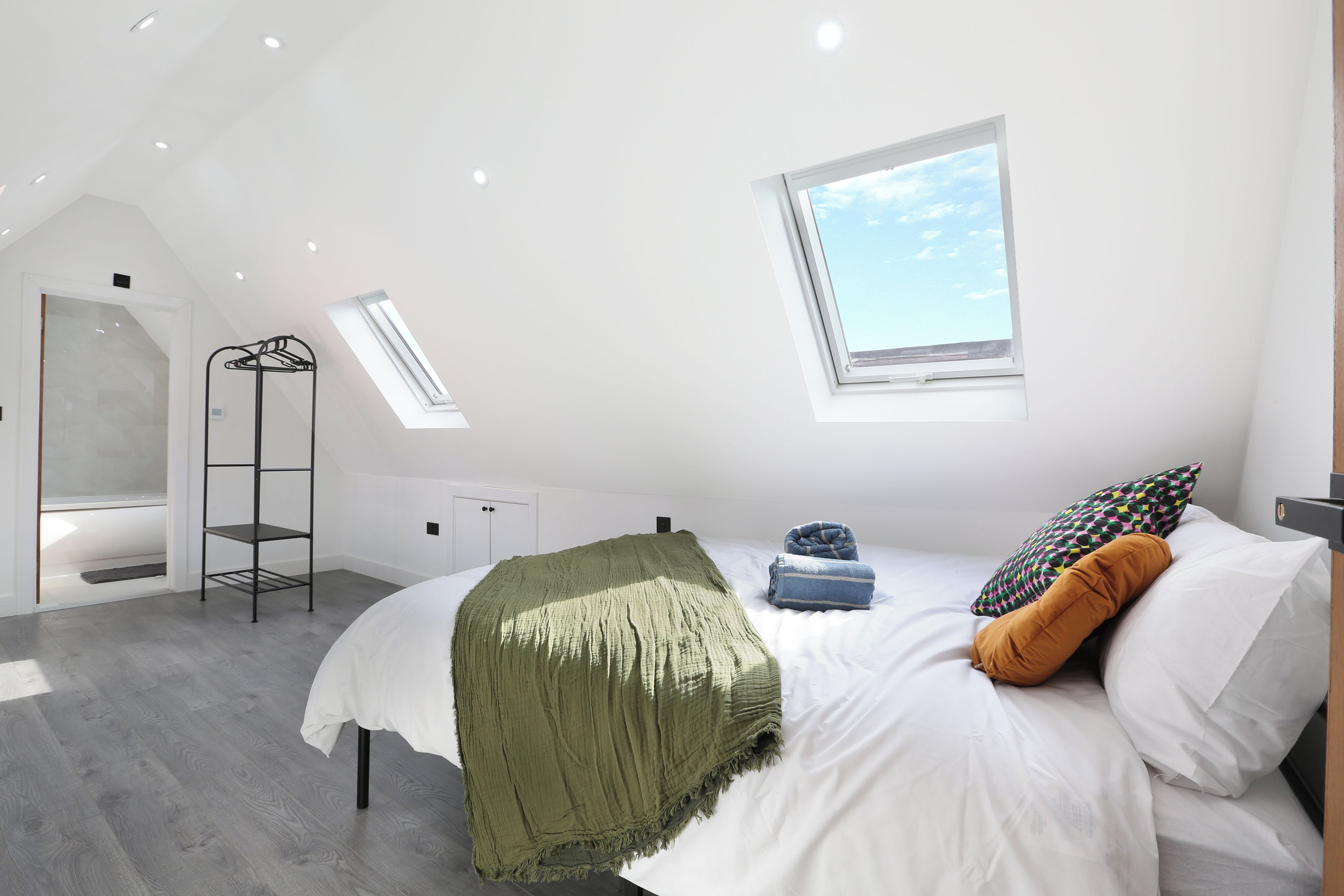 A modern bedroom with a skylight, a bed with pillows, a hanging shelf, and a radiator.