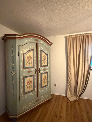 Ein Zimmer mit Holzboden, heller Wand und einem großen Schrank mit floralem Dekor.