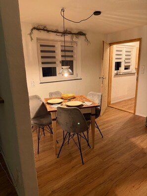 Ein Essbereich mit einem Tisch für vier Personen, zwei Stühlen, einer Hängelampe und einem Fenster mit Rollläden.
