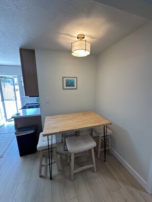 Un comedor con una mesa de madera y bancos, una cocina al fondo y una lámpara en el techo.