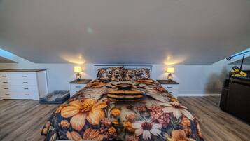 Ein Schlafzimmer mit blumigem Überwurf, zwei Nachttischlampen, einem Schminktisch und einem kleinen Tisch mit einem dekorativen Gegenstand.